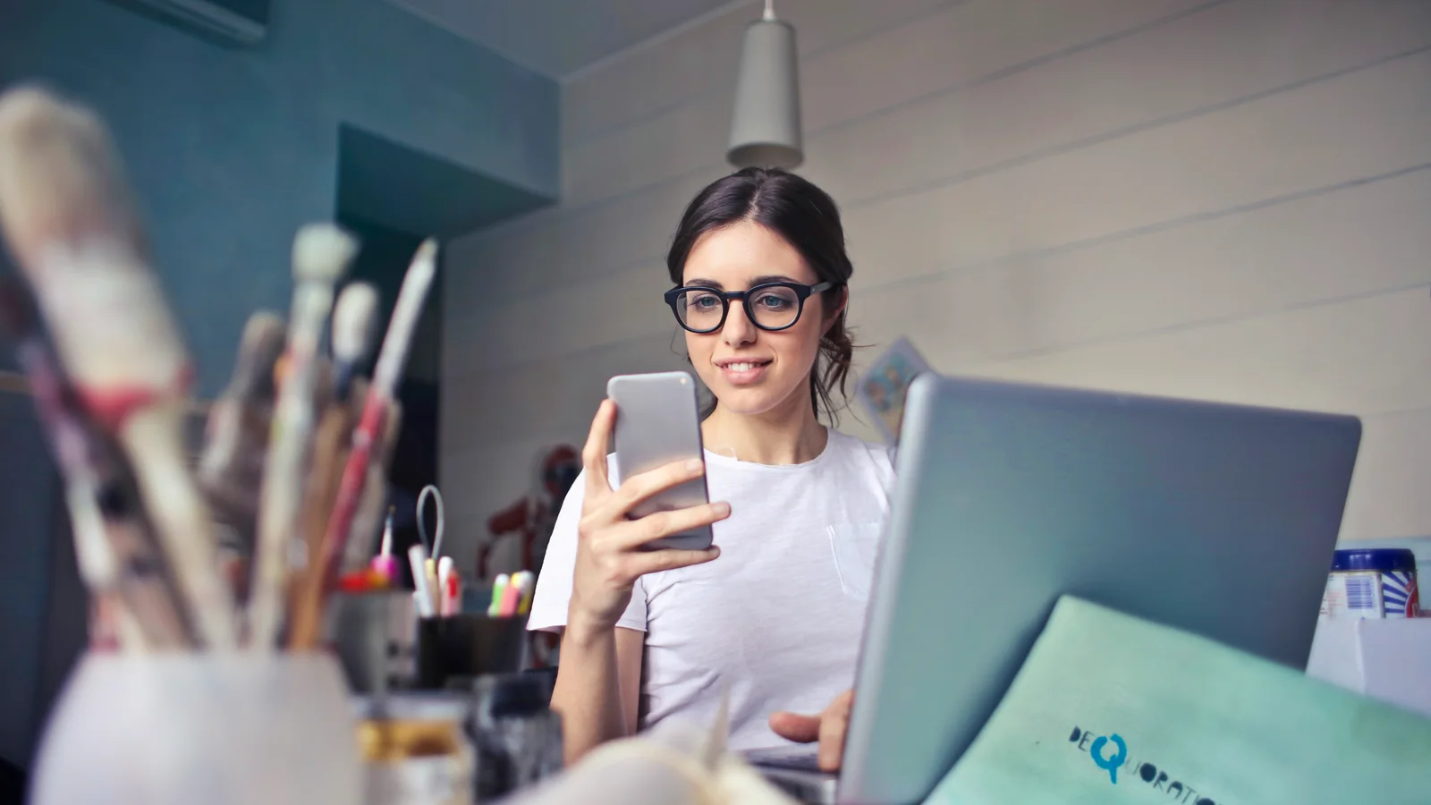 Mujer consultando su teléfono junto a una computadora portátil