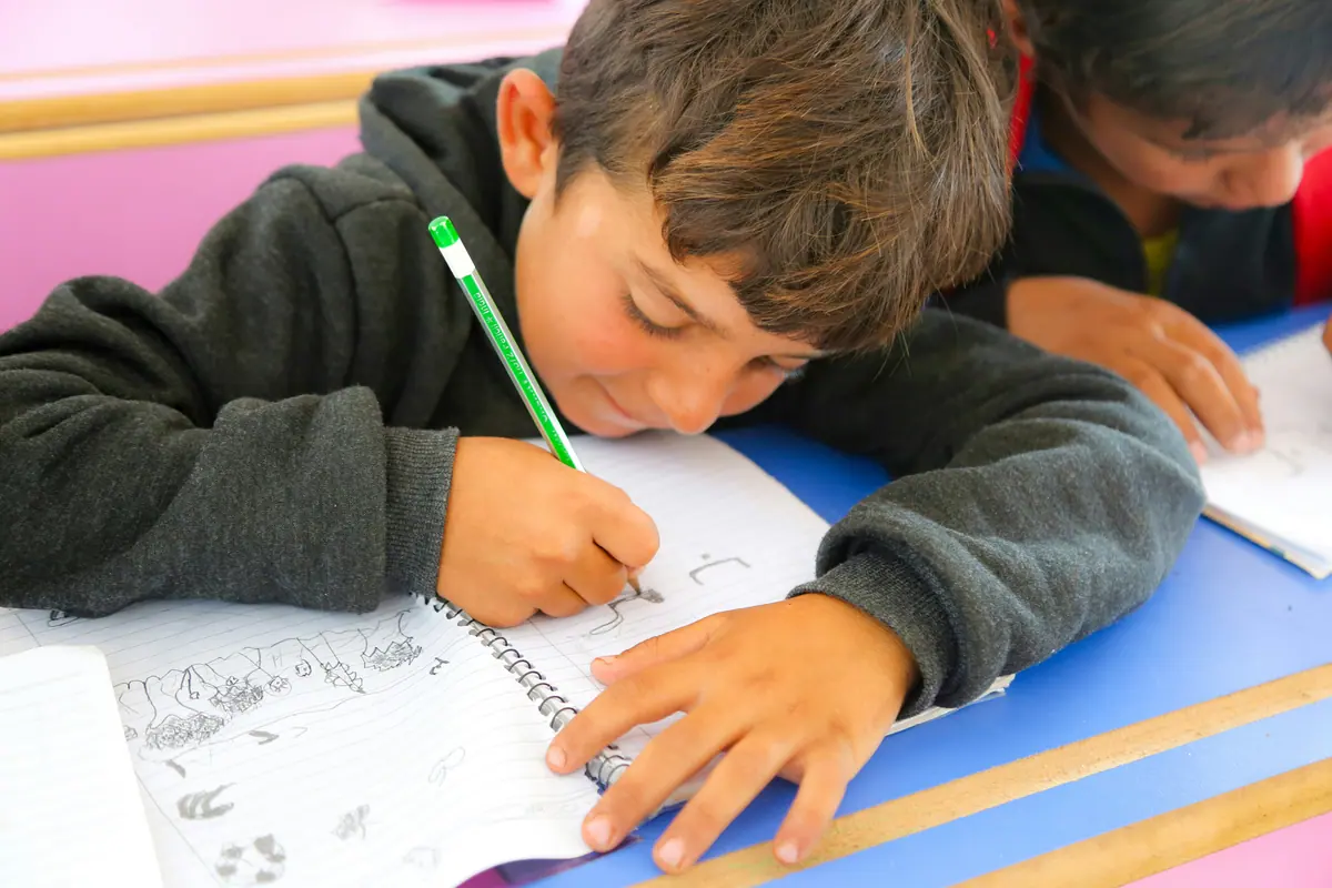 Estudiante escribiendo con atención sobre una hoja de trabajo